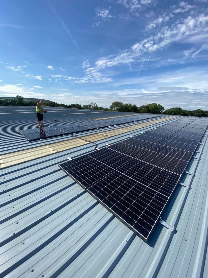 Simply Solar installer fitting solar panels on a commercial roof under a clear blue sky